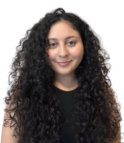 A young latina woman with dark brown curly hair and brown eyes wearing a black t-shirt smiles at the camera in front of a white background.